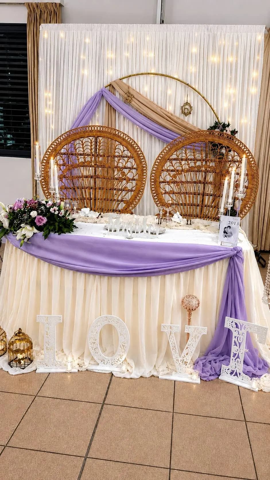 Voilages lilas et ivoire, fleurs et fauteuils en rotin autour d’une table décorée